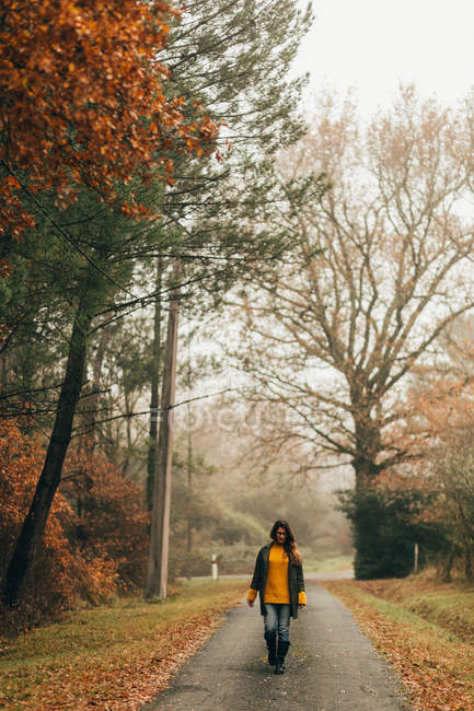 Donna a piedi su strada nei boschi autunnali — Foto stock