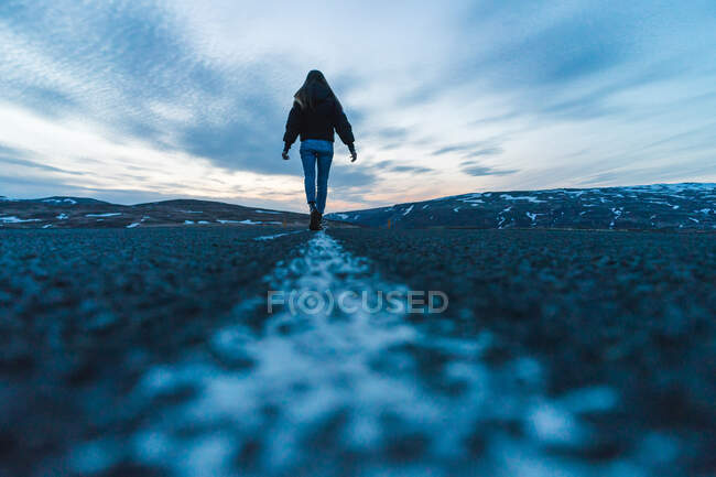 Vista laterale della giovane donna in piedi in mezzo alla strada in posa difficile e indicando a sinistra durante il viaggio attraverso l'Islanda. — Foto stock