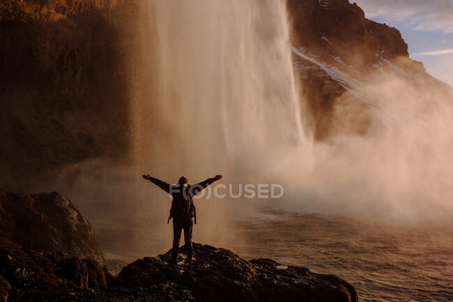 Back view of tourist standing with hands apart at waterfall in Iceland. — Stock Photo