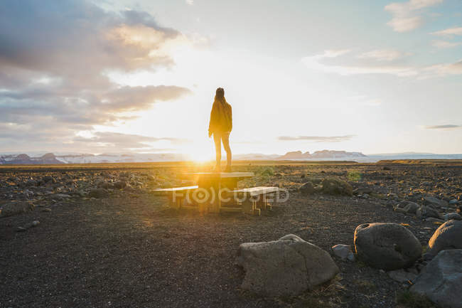 Жінка стоїть на дерев'яному столі на заході сонця — стокове фото