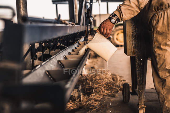 Agricultor vertiendo leche a la máquina de alimentación - foto de stock
