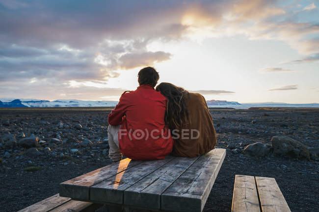 Couple sitting on wood table at sunset — Stock Photo