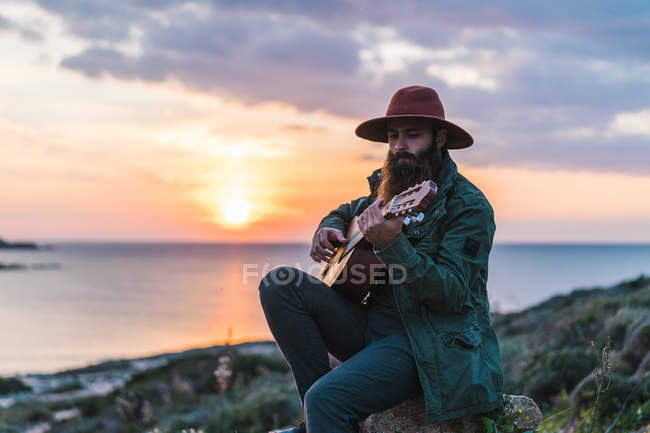 Чоловік сидить з гітарою на узбережжі — стокове фото