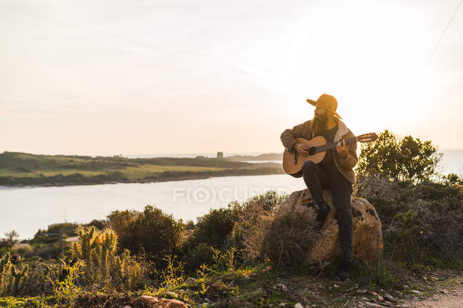 Man playing guitar on rock — Stock Photo