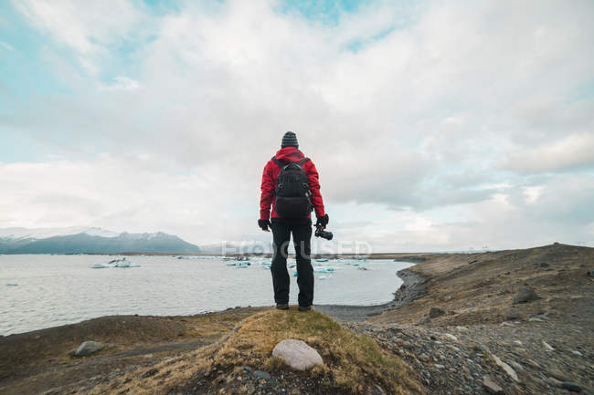 Hombre de pie en el lago con cámara - foto de stock
