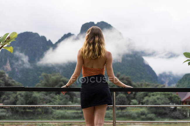 Жінка спирається в поручнях, дивлячись на гори — стокове фото