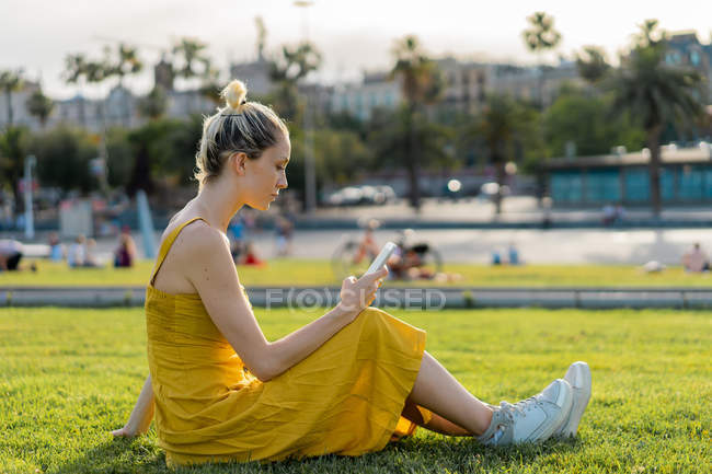 Mulher sentada na grama na cidade com smartphone — Fotografia de Stock