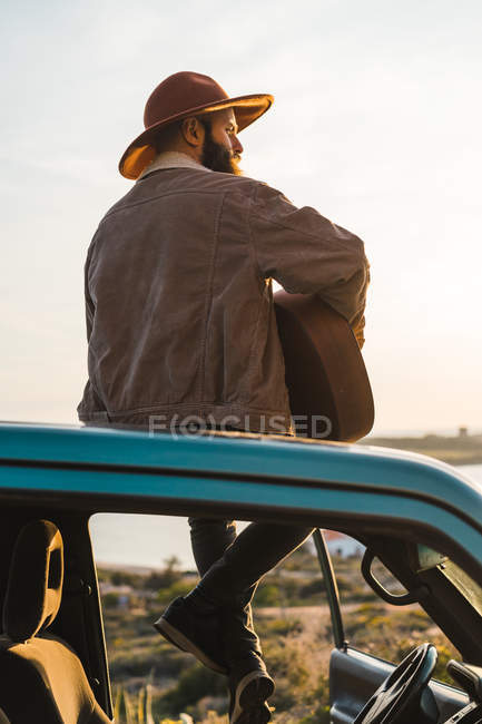 Uomo seduto sul tetto dell'auto al mare — Foto stock
