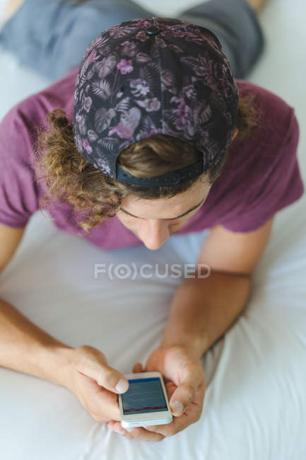 Homme utilisant un smartphone sur le lit — Photo de stock