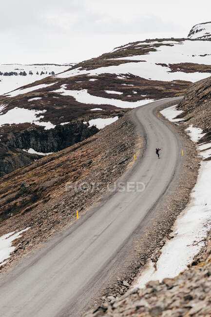 Aerial view of traveler riding skate on long remote road in snowy mountains of Iceland. — Stock Photo