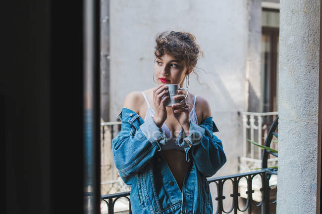 Frau in Jeansjacke mit Pokal auf Balkon — Stockfoto