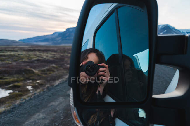 Отражение молодой женщины с камерой в зеркале заднего вида автомобиля во время поездки по Исландии. — стоковое фото