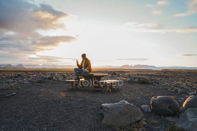 Woman sitting on wooden table at sunset — Stock Photo