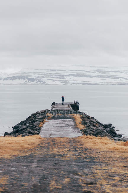Vue arrière de l'homme avec caméra debout sur la jetée contre la plage enneigée dans la brume, Islande. — Photo de stock