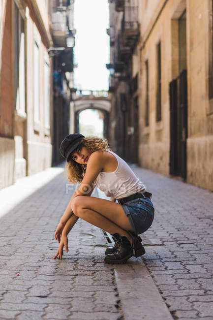Mujer con botas y gorra sentada en la calle - foto de stock