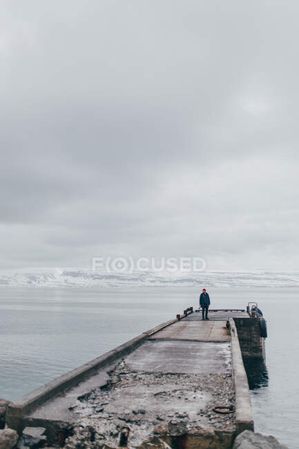 Homme debout sur une jetée de pierre humide dans la mer sombre avec des nuages sombres au-dessus, Islande. — Photo de stock