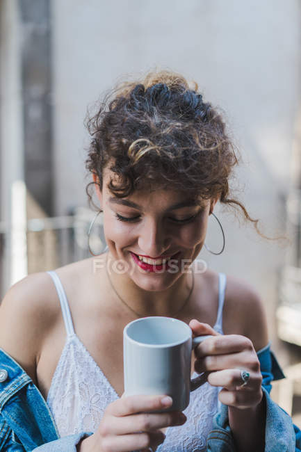 Кучерява жінка з чашкою кави на балконі — стокове фото