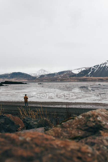 Blick auf eine Person am Ufer des zugefrorenen Sees mit Bergen im Hintergrund, Island. — Stockfoto