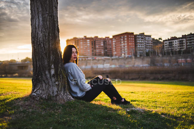 Donna seduta sotto l'albero alla luce del sole — Foto stock