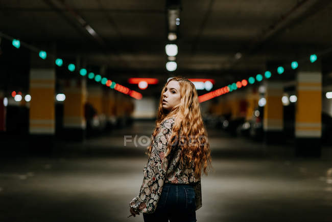 Pretty redhead woman smoking while walking on blurred parking lot — Stock Photo