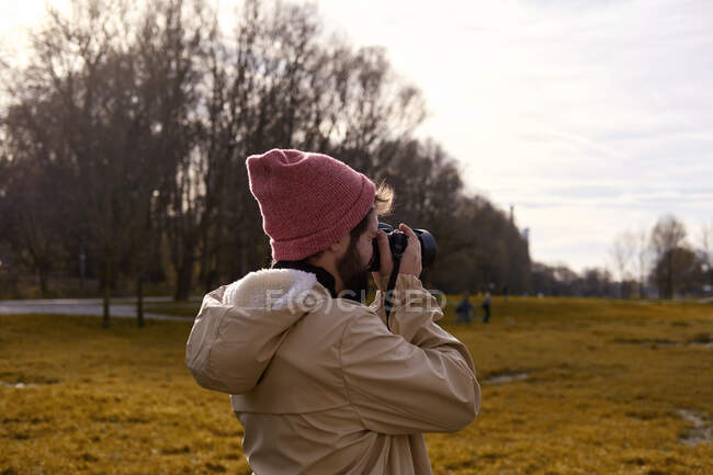 Vista lateral del fotógrafo de pie y tomando fotos en el parque en Munich - foto de stock