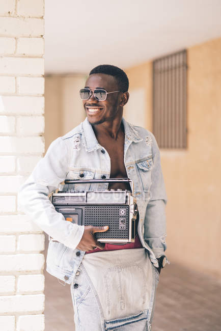 Улыбающийся черный мужчина в солнечных очках держит винтажное радио устройство на открытом воздухе — стоковое фото