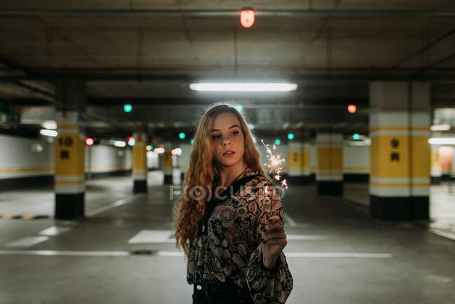 Junge Frau steht mit Wunderkerze auf Parkplatz — Stockfoto