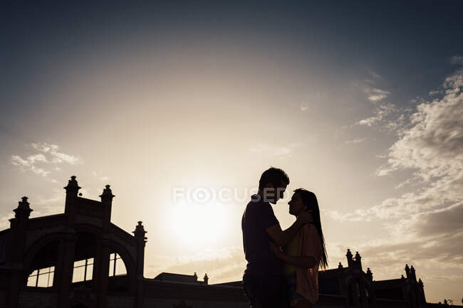 Vista laterale di silhouette di giovane coppia in piedi e abbracciando nel parco. — Foto stock