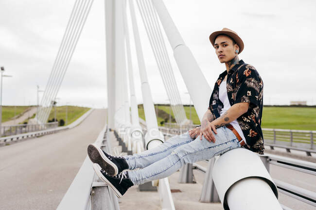 Hipster sentado en la barandilla del puente - foto de stock