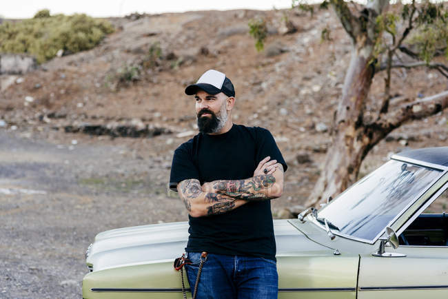 Татуированный мужчина, опирающийся на машину — стоковое фото