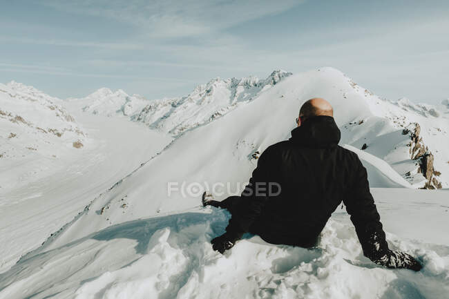 Vue arrière d'un homme adulte sans poils assis sur une montagne enneigée en hiver, Glaciar Aletsch desde el viewpoint de Eggishorn en Fiesch, Suisse — Photo de stock