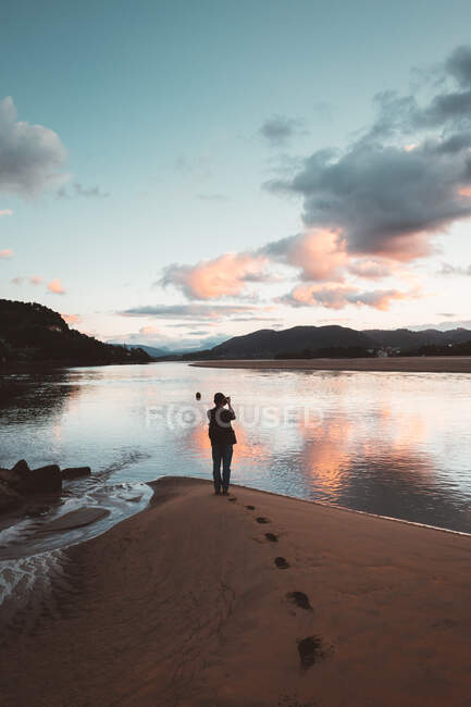 Back view of photographer on sandy beach of Laida with colorful sky reflecting in water, Bizkaia - foto de stock