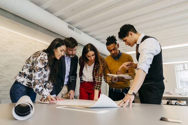 Multiethnic office team standing at the table while working on the blueprint. — Stock Photo