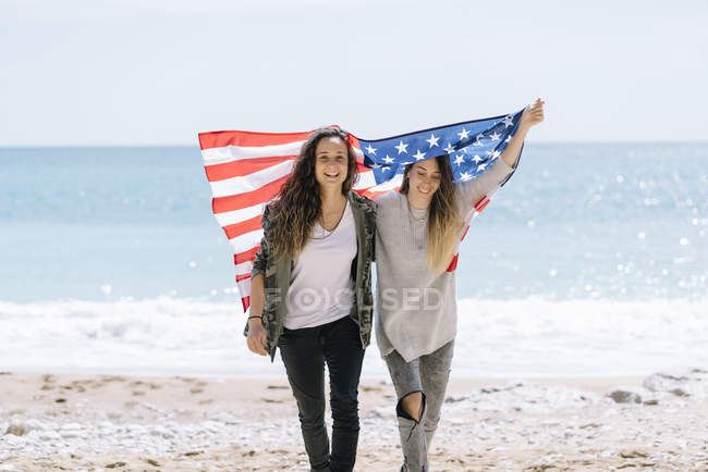 Deux jeunes femmes adultes posant sur la plage avec drapeau des États-Unis . — Photo de stock
