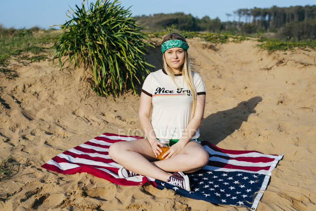 Chica con bebida sentado en la bandera americana - foto de stock