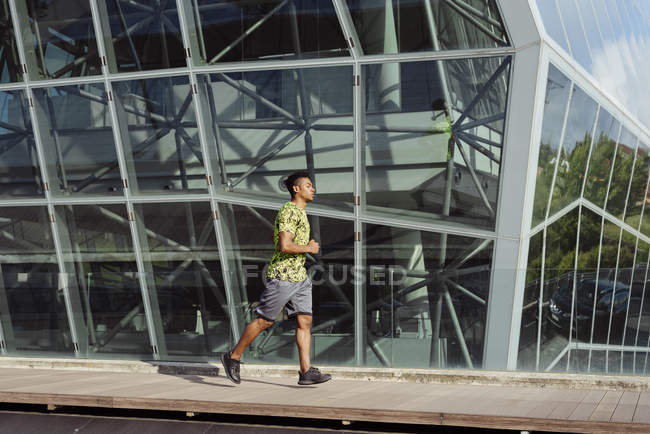 Ethnic man jogging against modern building in city — Stock Photo