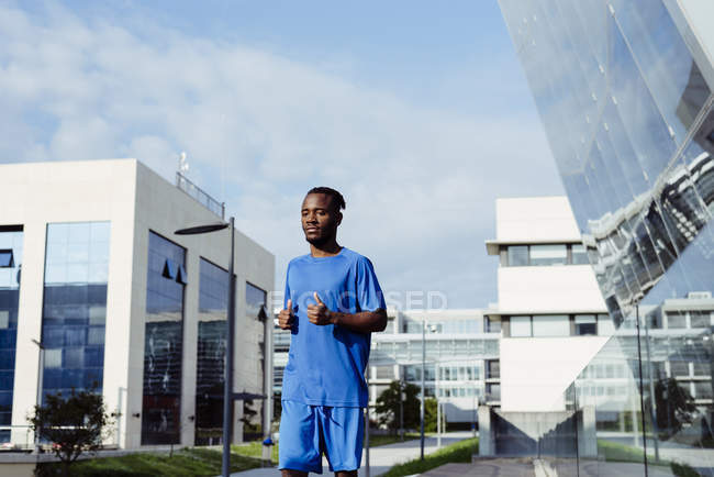 Ethnischer Mann joggt in der Stadt mit modernen Gebäuden im Hintergrund — Stockfoto