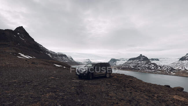 Grande voiture moderne hors route garée sur le rivage au bord du lac dans les montagnes enneigées en Islande — Photo de stock