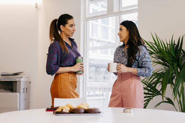 Hübsche junge Frauen stehen zusammen und unterhalten sich in der Kaffeepause im Büro. — Stockfoto