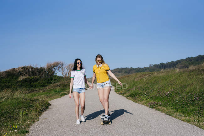 Female friends with skateboard on rural road — Stock Photo