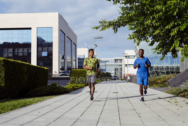 Ethnic men jogging together on modern street — Stock Photo