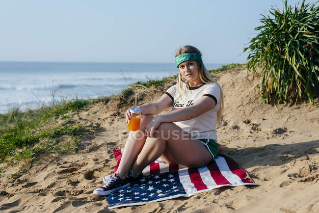 Chica con bebida sentado en la bandera americana - foto de stock