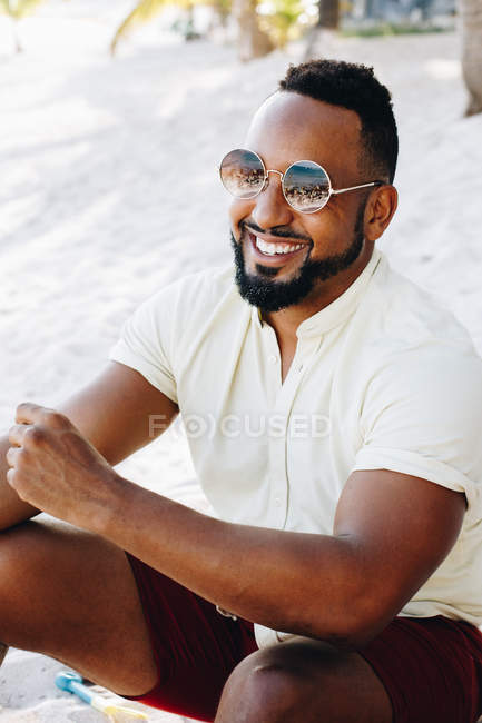 Людина в сонцезахисних окулярах сидить на пляжі — стокове фото