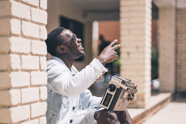 Happy black man in sunglasses holding vintage radio device outdoors — Stock Photo