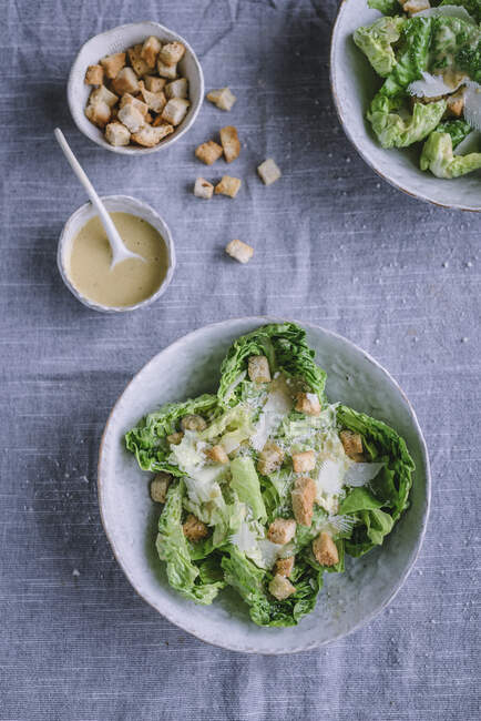 Schüsseln mit knusprigen Croutons und frischer Soße stehen neben köstlichem Salat auf grauem Tuch. — Stockfoto