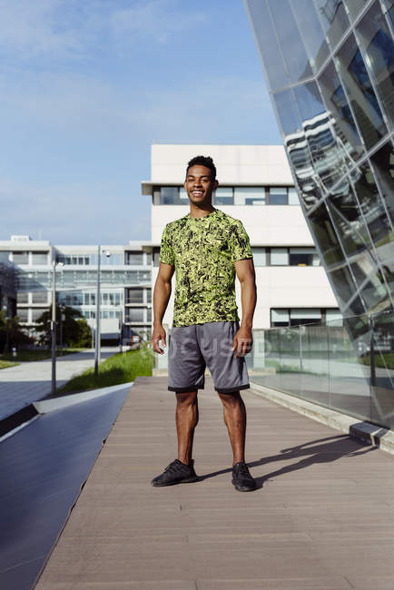 Bello sportivo uomo etnico in piedi in città con edifici moderni sullo sfondo — Foto stock