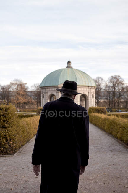Vista trasera del hombre adulto mayor con estilo en abrigo y sombrero de pie en el parque en Munich - foto de stock