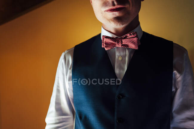 Crop young man in waistcoat with red bow tie on background of yellow wall. — Stock Photo
