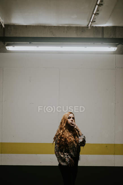 Femme rousse rêveuse fumant devant le mur — Photo de stock