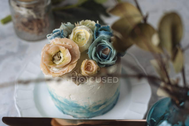Свадебный торт с голубыми и бежевыми цветами из сливочного масла на белой тарелке — стоковое фото